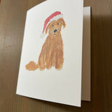 Card with a dog wearing a Santa hat on a wooden surface